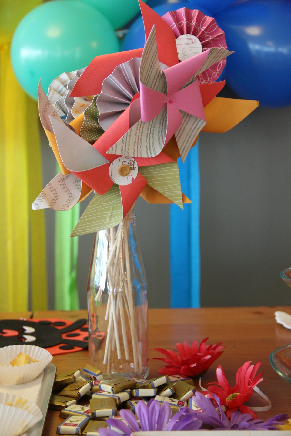 Molinetes de papel en un frasco entre bocadillos y decoraciones de fiesta.